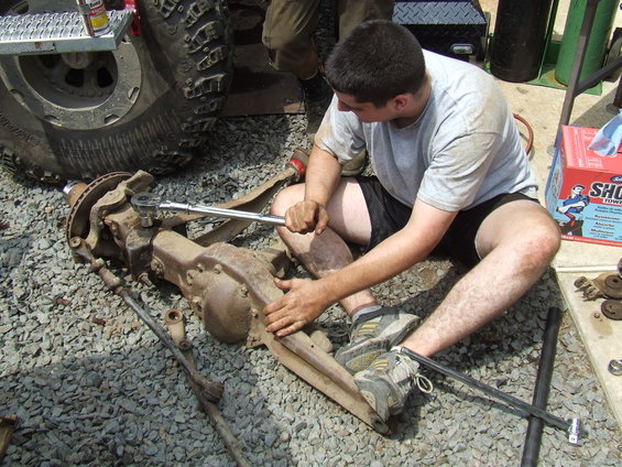 Front axle assembly with suspension components and a man working on it with a socket wrench