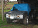1968 Ford Bronco - A 1968 Ford Bronco is partially covered by a blue tarp while parked in a rustic shelter.