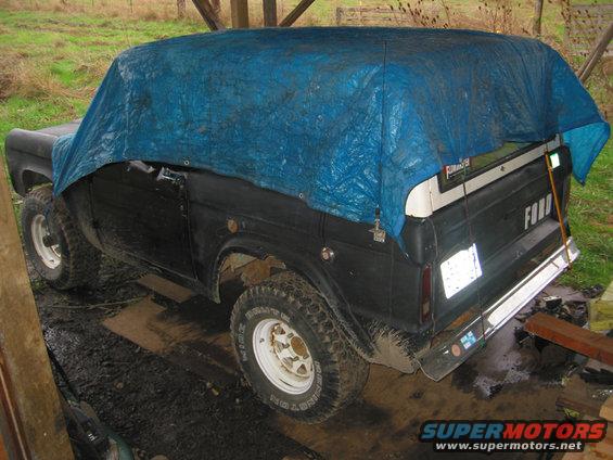 Black Ford Bronco covered by a blue tarp, seen from the 3/4 front angle