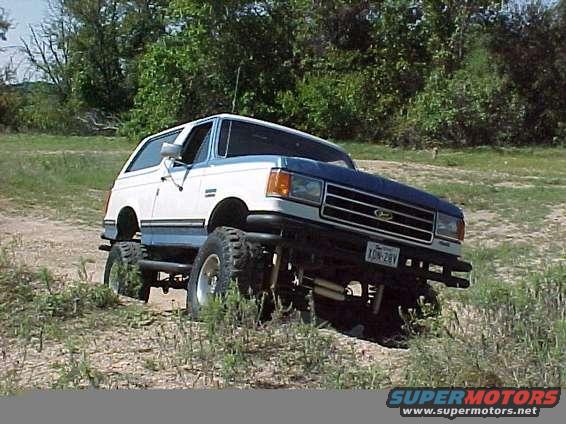 1990 Ford Bronco, 3q-front view, white and blue, lifted for off-roading. License plate XON-28V