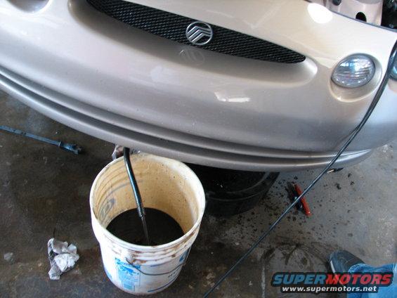 Gold 1998 Mercury Sable front end with a bucket of dark fluid draining from underneath