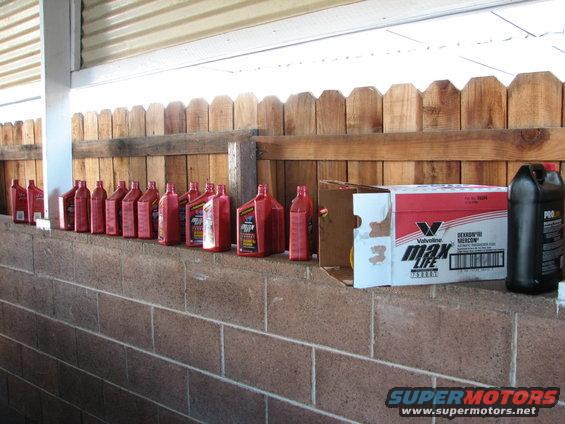 Row of red transmission fluid bottles, a Valvoline MaxLife box, and a black fluid bottle on a brick ledge