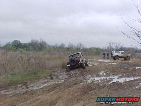 Two off-road vehicles navigating a muddy terrain under an overcast sky