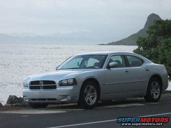 Silver 2006 Dodge Charger parked on a road next to the ocean with a mountain in the background