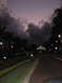 2006 Dodge Charger - Night scene with dramatic clouds over a road and a distant building, flanked by palm trees.