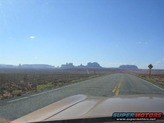 Car hood perspective on desert highway with mesas in distance
