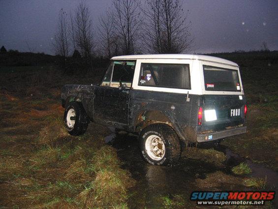 1968 Ford Bronco parked in muddy field with trees in background