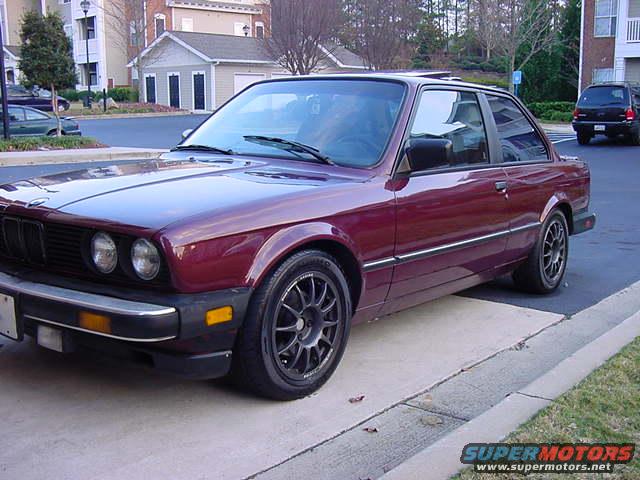 maroon coupe parked on concrete, black SUV in background