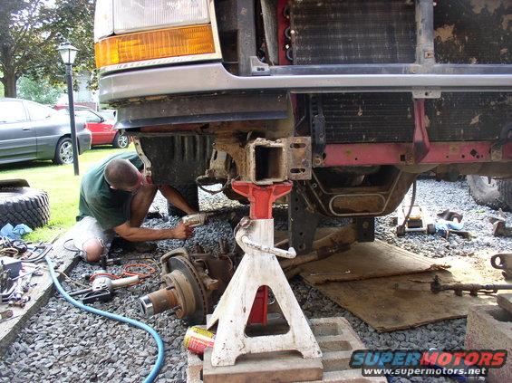Man working on the front end of a 1996 Ford F-250, with the bumper removed and parts on jack stands