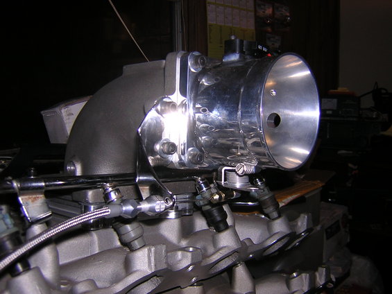 Close-up of a chrome throttle body attached to a grey engine manifold with fuel injectors