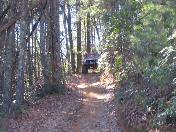 Red off-road vehicle with large tires on a narrow dirt path through a forest