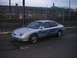 1999 Ford Taurus - This sedan features custom blue flame decals on its side, parked in an asphalt lot with a chain-link fence in the background.
