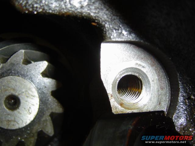 Close-up of a metal gear with teeth and a threaded hole in a metal housing