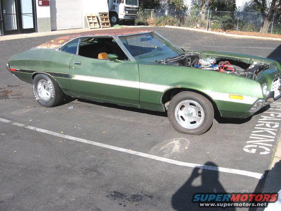 Green coupe, hood up, showing engine. White stripe along side. Flat front tire