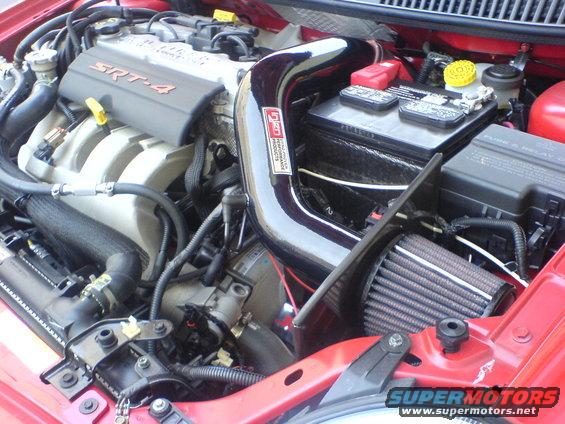 Red 2005 Dodge SRT-4 engine bay with SRT-4 branded engine cover, aftermarket intake, and battery