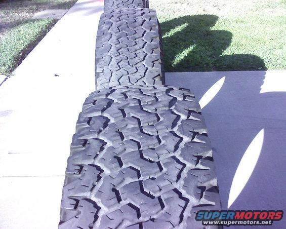 Four off-road tires stacked on a sidewalk