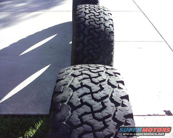 Stack of off-road tires on a concrete surface with grass and shadows