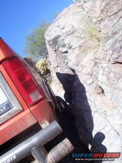 Orange SUV's rear quarter panel and taillight close to a large rock formation