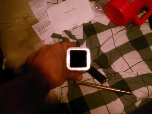 Hand holding a square metal tube with a rod and a red mug in the background