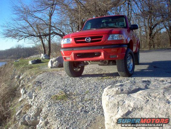 Red Mazda B3000 pickup truck parked on a gravelly area near some trees and water