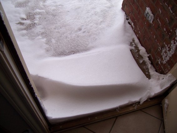 Snowdrift covering a doorway and part of a brick wall