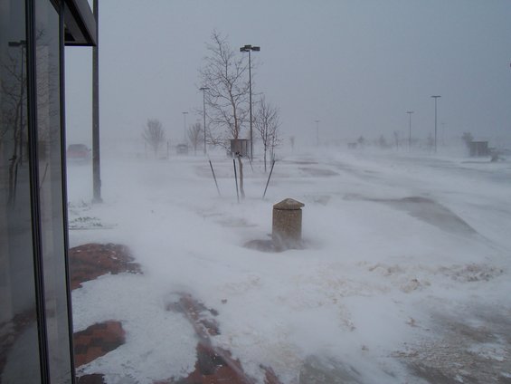 Parking lot obscured by blowing snow, with a red car visible in the distance