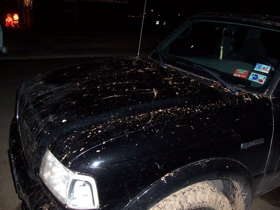 Black Ford Ranger pickup truck covered in mud, front fender and hood visible