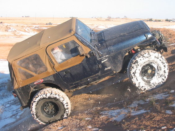 Black Jeep Wrangler TJ with tan soft top on snowy, muddy terrain