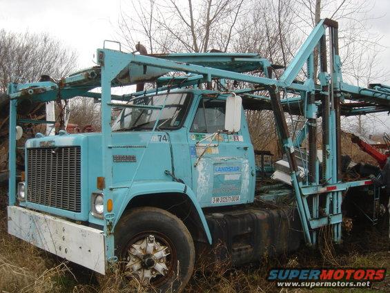 Blue car carrier truck with 'BRIGADIER' and 'LANDSTAR' decals, parked in tall grass