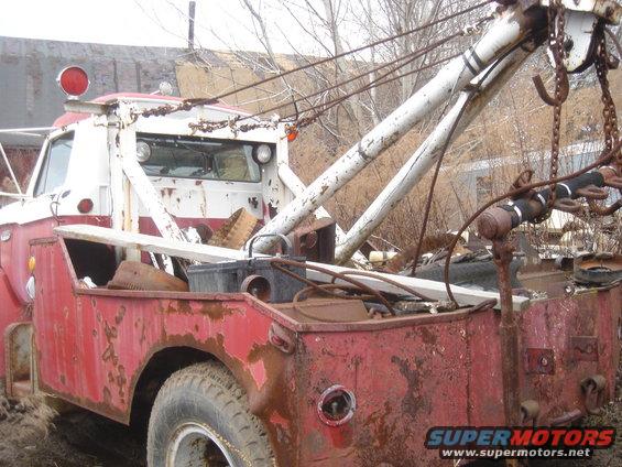 Red and white tow truck with rust, rear view, showing tow equipment and debris