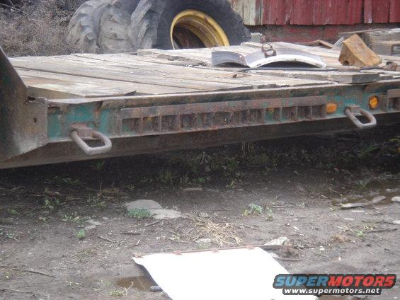 Flatbed trailer with tie-down rings and a large tractor tire in the background
