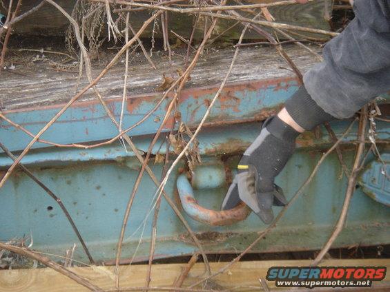 Rusty blue truck bed section with a hook being touched by a gloved hand