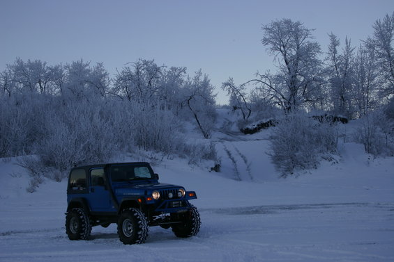 Blue 2003 Jeep TJ parked in snow with frosted trees and a snowy hill in background