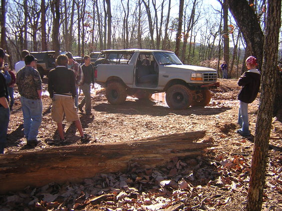 Gray Ford Bronco with doors open, mud tires, off-roading with people around. Another SUV visible in background