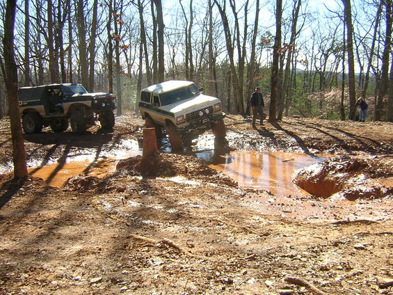White Ford Bronco navigating a muddy trail with a second Bronco behind it