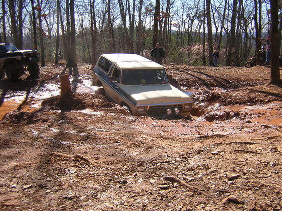 Tan and blue Ford Bronco stuck in deep mud, front view