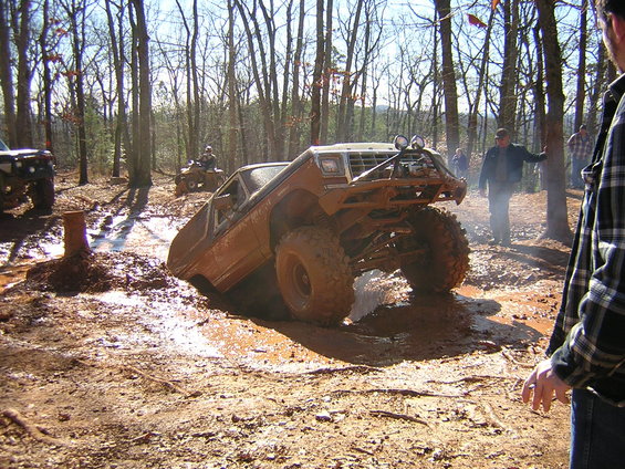 off-road vehicle stuck in mud pit, another vehicle and ATV in background