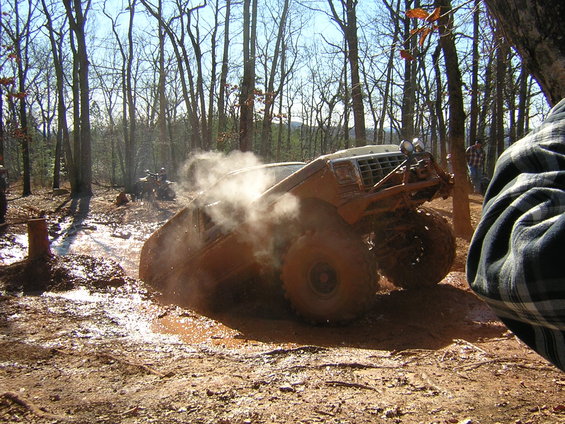 1979 Ford Bronco stuck in mud, kicking up dust. Another ATV visible in background