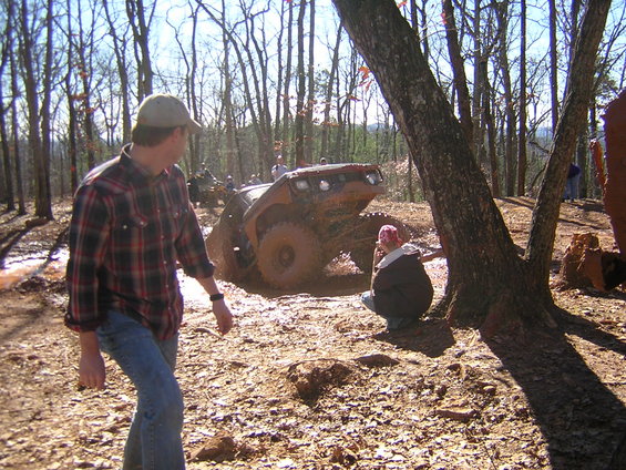 Off-road vehicle stuck in mud pit with people watching