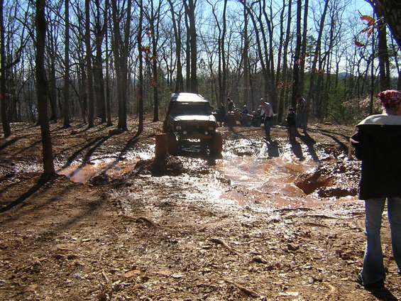 Brown off-road vehicle with lifted suspension navigating a muddy trail, front view