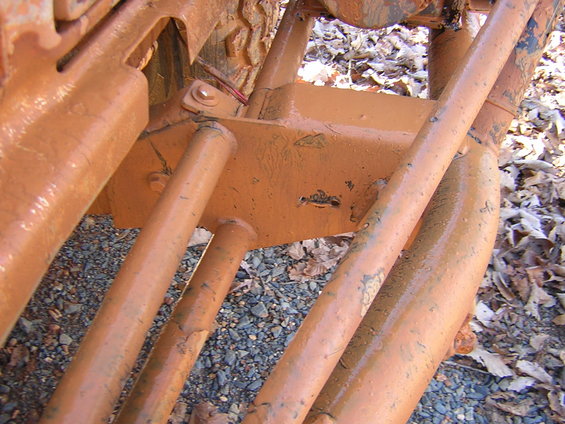 Close-up of orange-painted suspension parts on a vehicle, with gravel and leaves on the ground