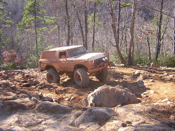Muddy 1978 Ford Bronco with lifted suspension and large tires navigating a rocky trail