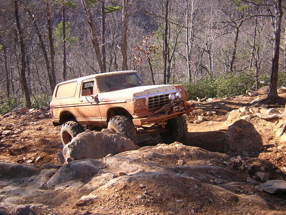 Orange off-road SUV climbing over rocks on a dirt trail