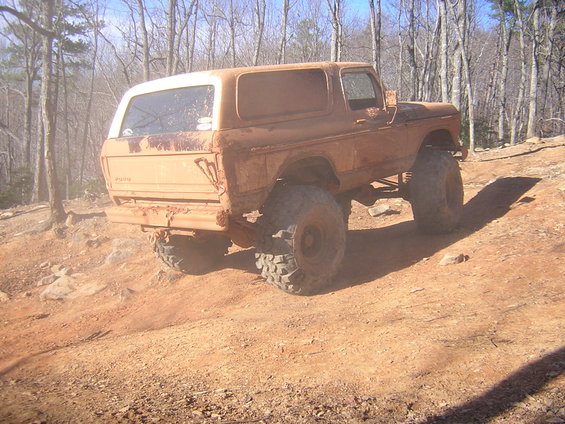 Mud-covered 1978 Ford Bronco with large off-road tires on a dirt trail