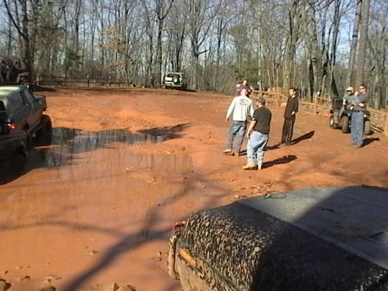 Muddy off-road vehicles and people gathered in a wooded area