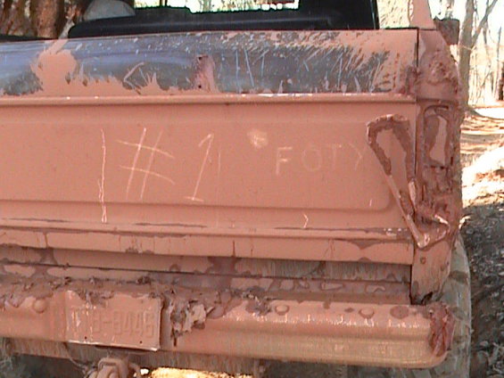 Mud-covered truck tailgate with '#1' and 'FOTY' written on it. License plate is visible