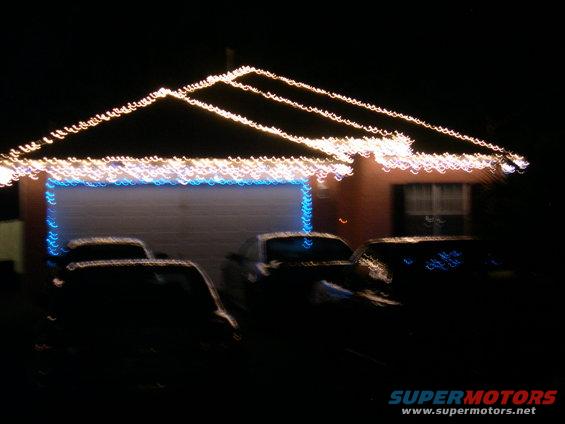 Cars parked in front of a house with Christmas lights on the roofline