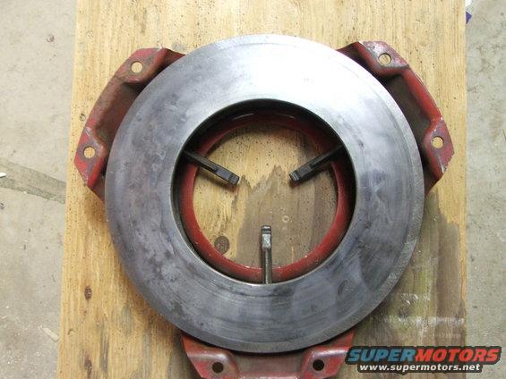 Clutch pressure plate with red housing and metal disc, mounted on wood
