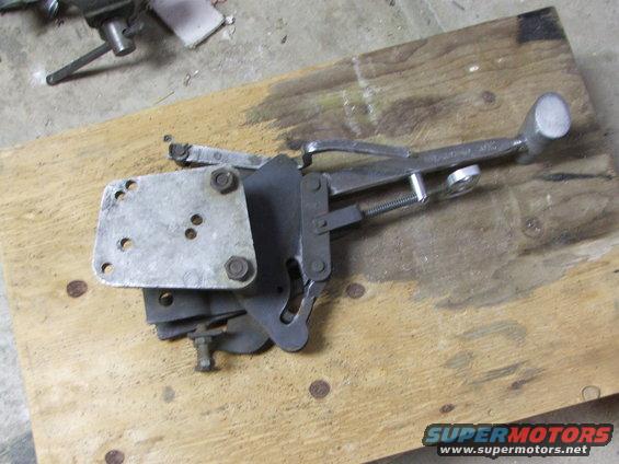 carburetor linkage assembly with a metal plate and bolts, resting on a wooden board