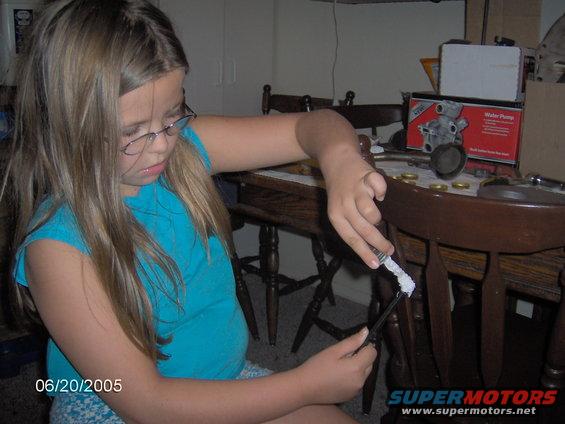 Girl with glasses applying white paste to a black tool near a "Water Pump" box